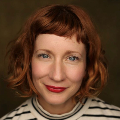 Bettrys Jones' headshot. She is a white woman in her thirties. She has short, wavy auburn hair and has a fringe. She has blue eyes and wears red lipstick. She is smiling with her mouth closed and looking directly in the camera.