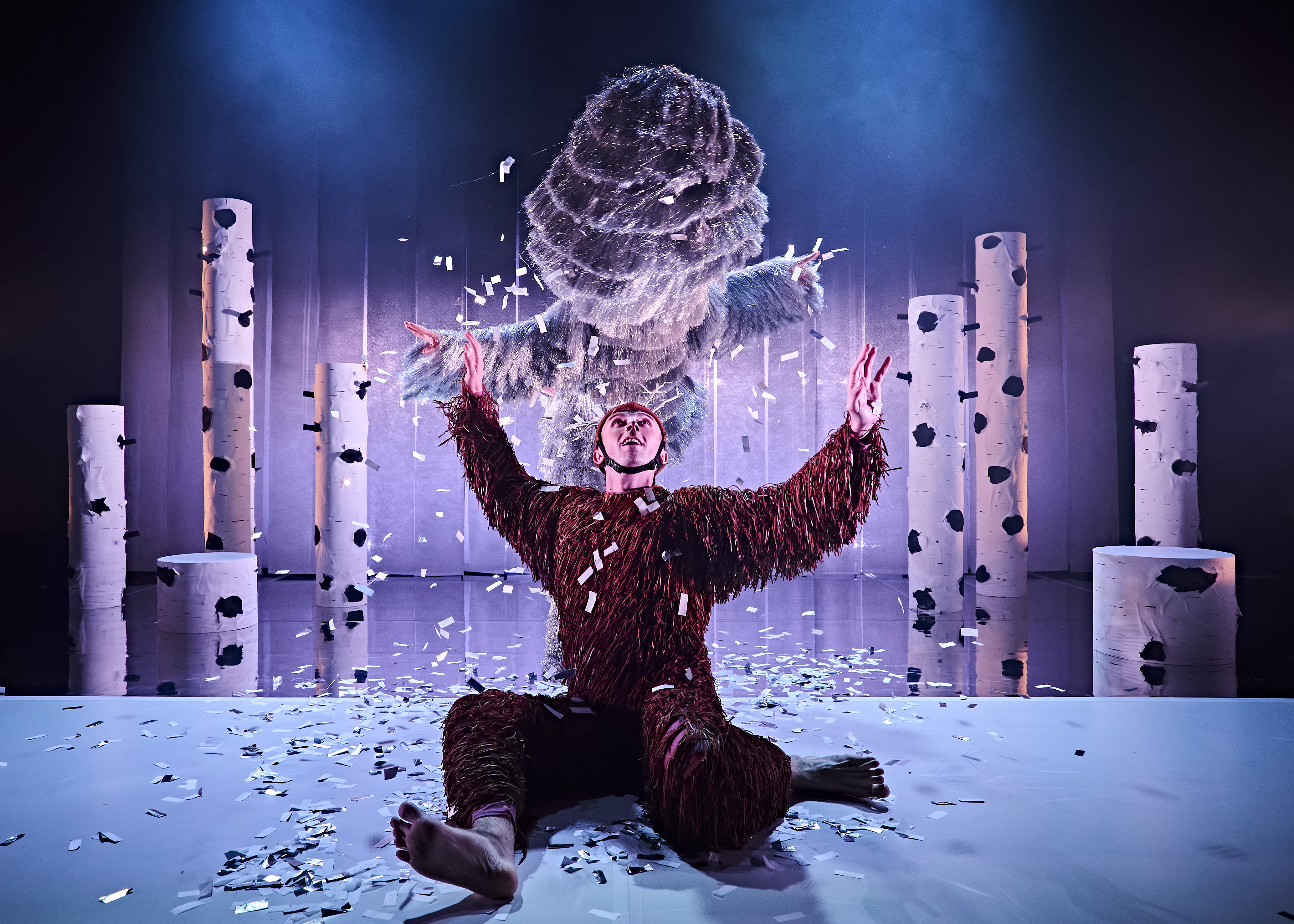 Production image from Dawns y Ceirw. A dancer dressed as a deer is being showered in confetti by a large snow storm.