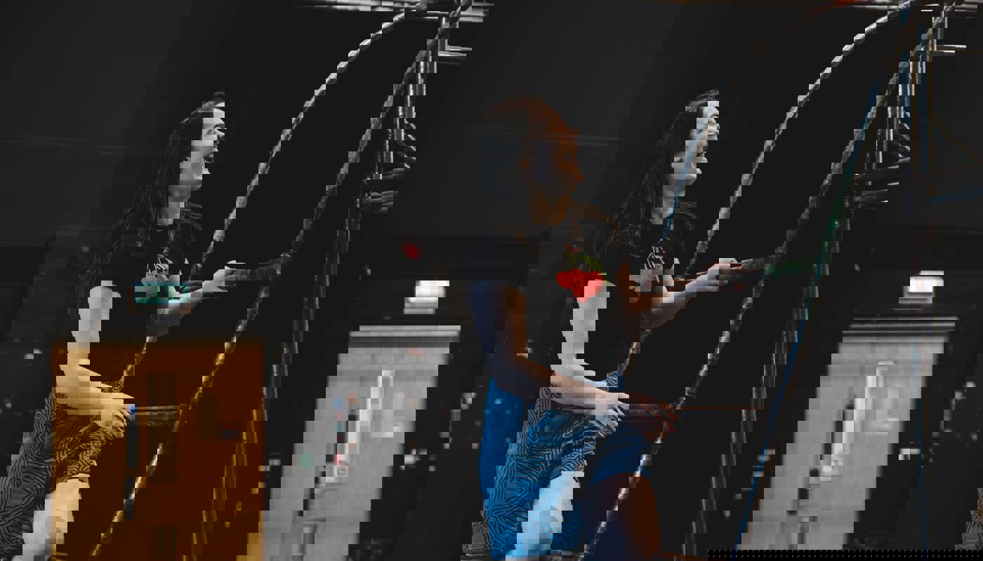 Young woman leans on an arching, small metal ladder. She is smiling with her teeth showing and looks up towards the top of the ladder