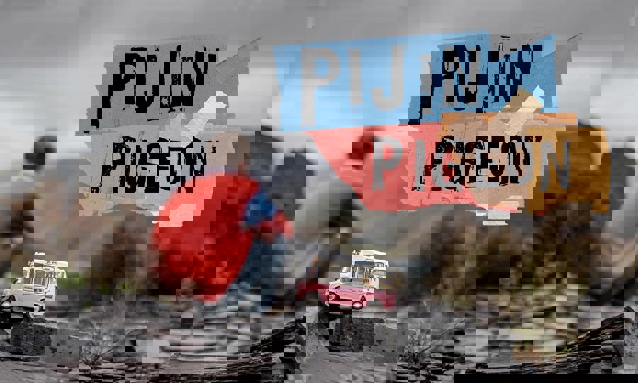 Exterior shot. The sky is grey and there are mountains in the background, unfocused. In front and in focus there is a pink and white small model ice cream van placed on a pile of small slates. Behind it out of focus a boy is sitting down with his back to the camera. Text on image reads ‘Pijin Pigeon’