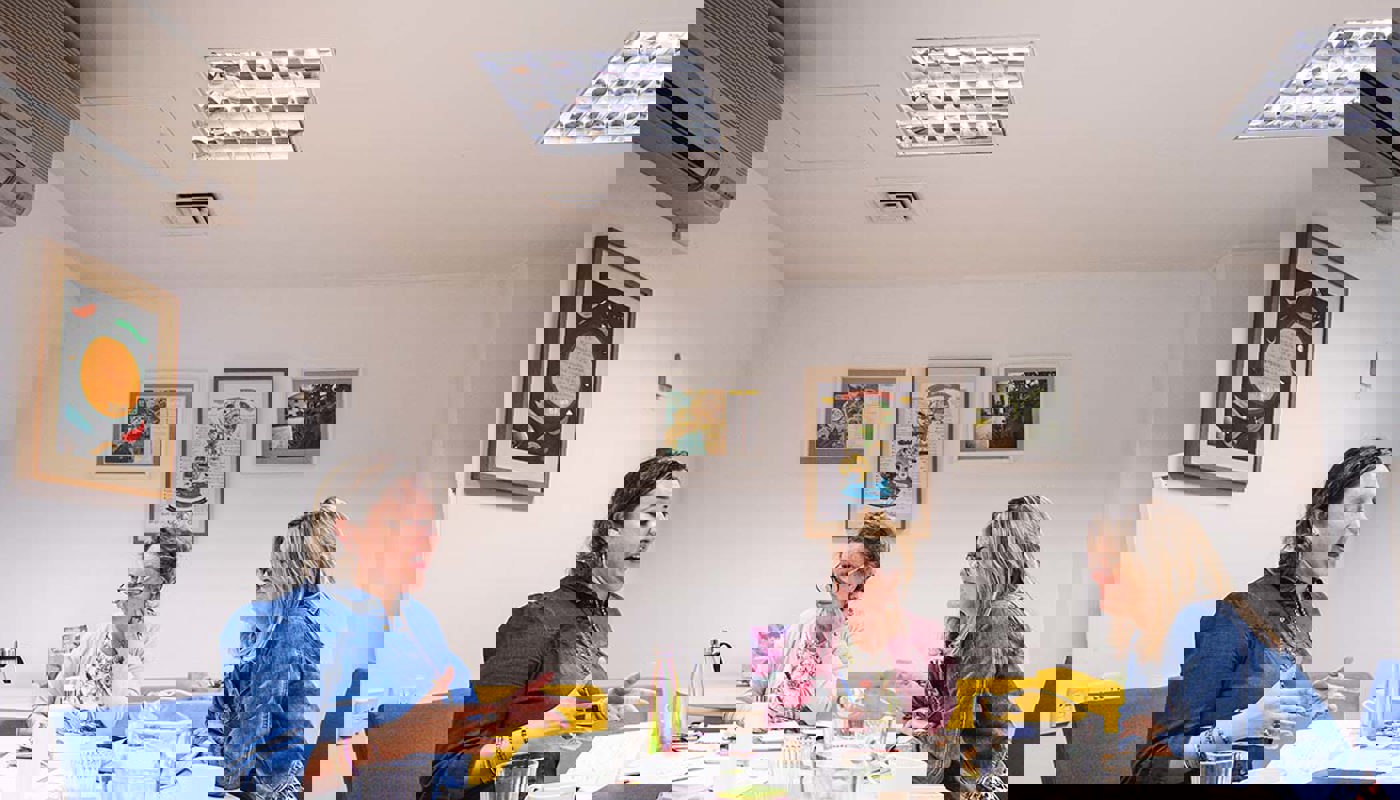 9.	Two middle-aged women and a younger woman sit around a table. The young woman has her mouth open, her hands are up and she is looking at a piece of paper on the table in front of her. The two other women are looking at the young woman.