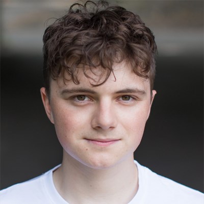 Headshot of Dewi Wykes. He is a young white male. He has short, slightly curly brown hair and brown eyes. He is staring directly into the camera and has a slight smile on his face.
