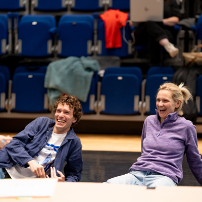 Rehearsal photo for Fy Enw i yw Rachel Corrie. A man and woman are sitting on the floor giggling.