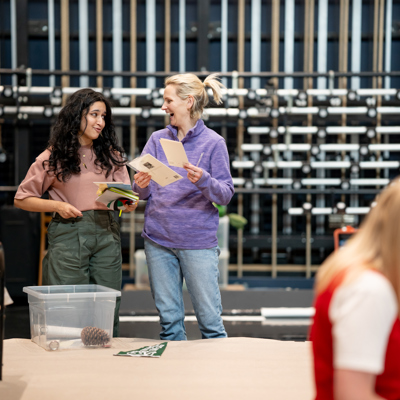 Rehearsal photo for Fy Enw i yw Rachel Corrie. Two women are looking at pieces of paper and giggling. 