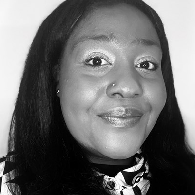 Stella-Jane's headshot in black and white. Stella is a black woman with long dark hair and brown eyes. She is smiling with her mouth closed and looks directly into the camera.