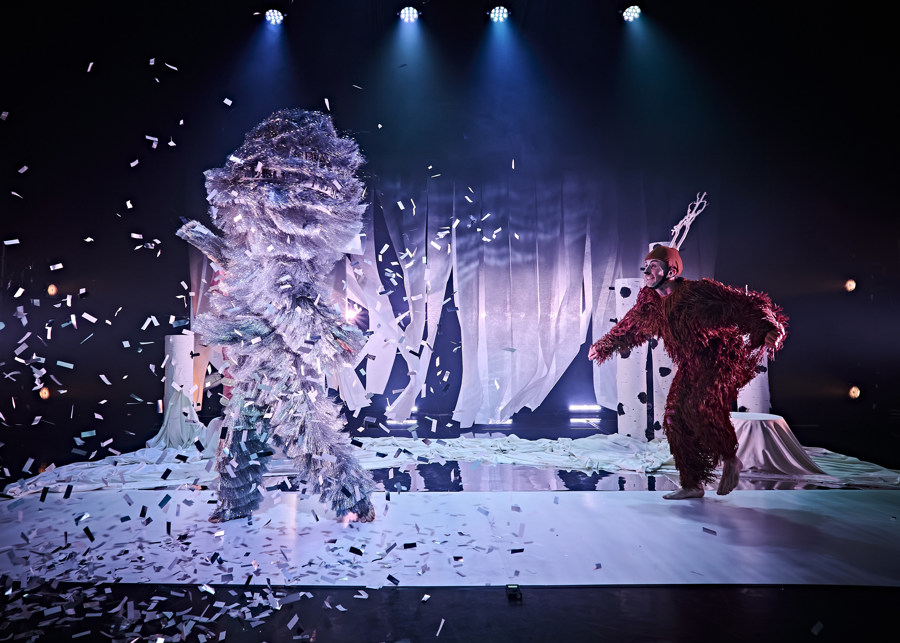 Production image from Dawns y Ceirw. A dancer dressed as a deer is being showered in confetti by a large snow storm.