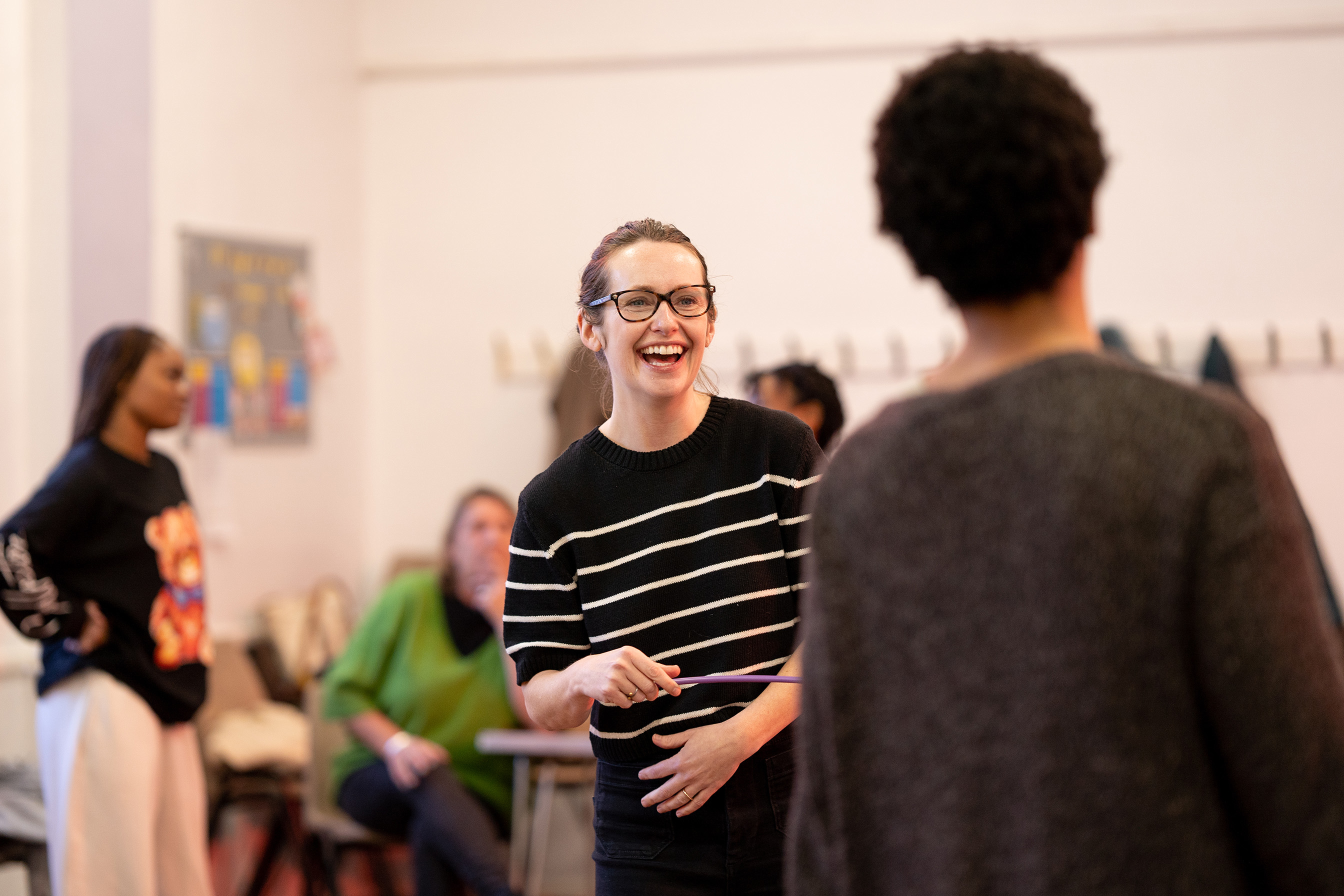 Image of Rhian Blythe in rehearsals. Rhian is a white woman in her forties. She has strawberry blonde hair tied back into a ponytail. She is wearing a black and white striped jumper. 
