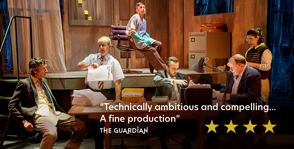 Review graphic. Production image featuring six actors in an office setting. Text on image reads 'technically ambitious and compelling...A fine production' The Guardian. 4 yellow stars are placed below the text.